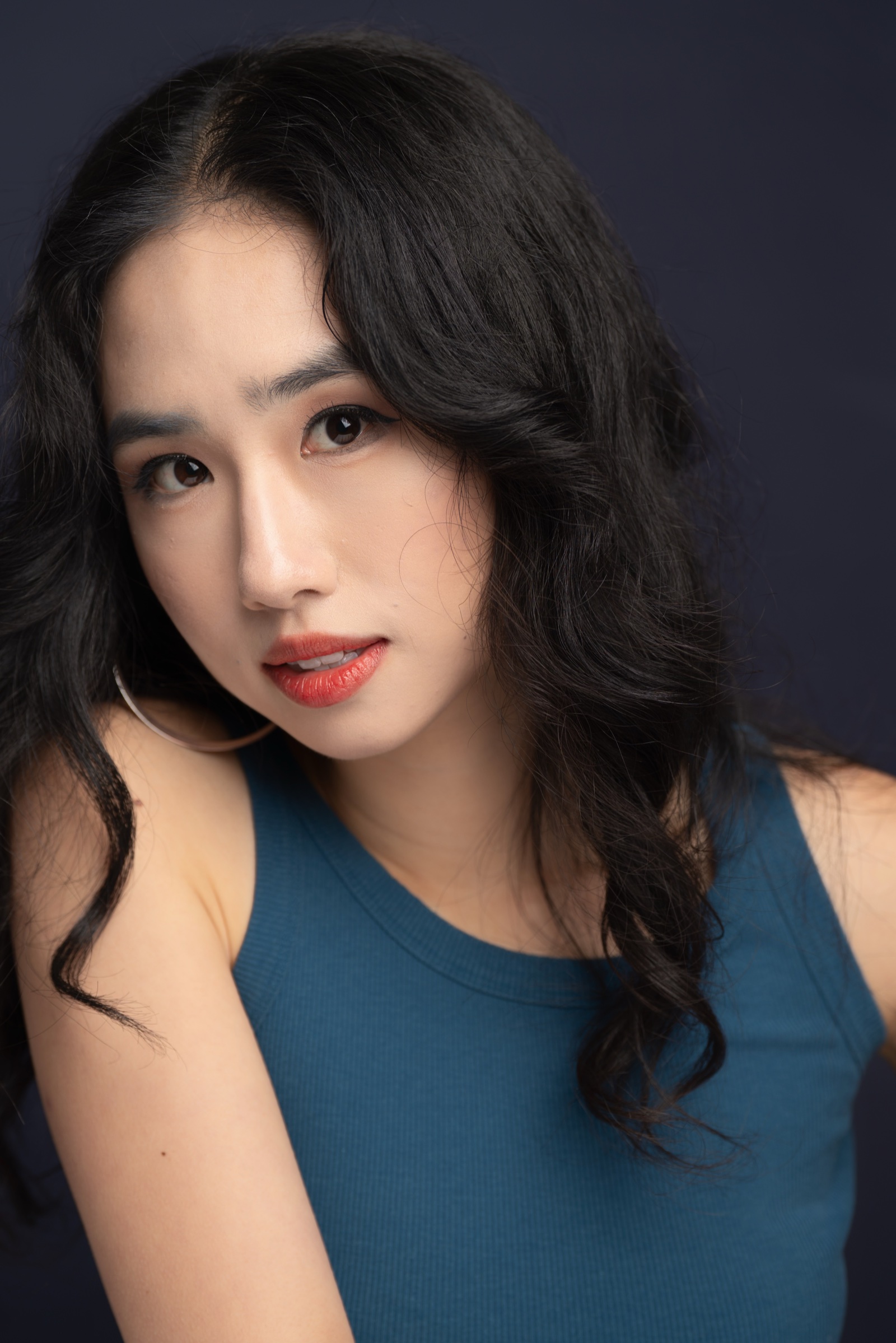 Minyi Zhang in a teal top against a navy studio backdrop.
