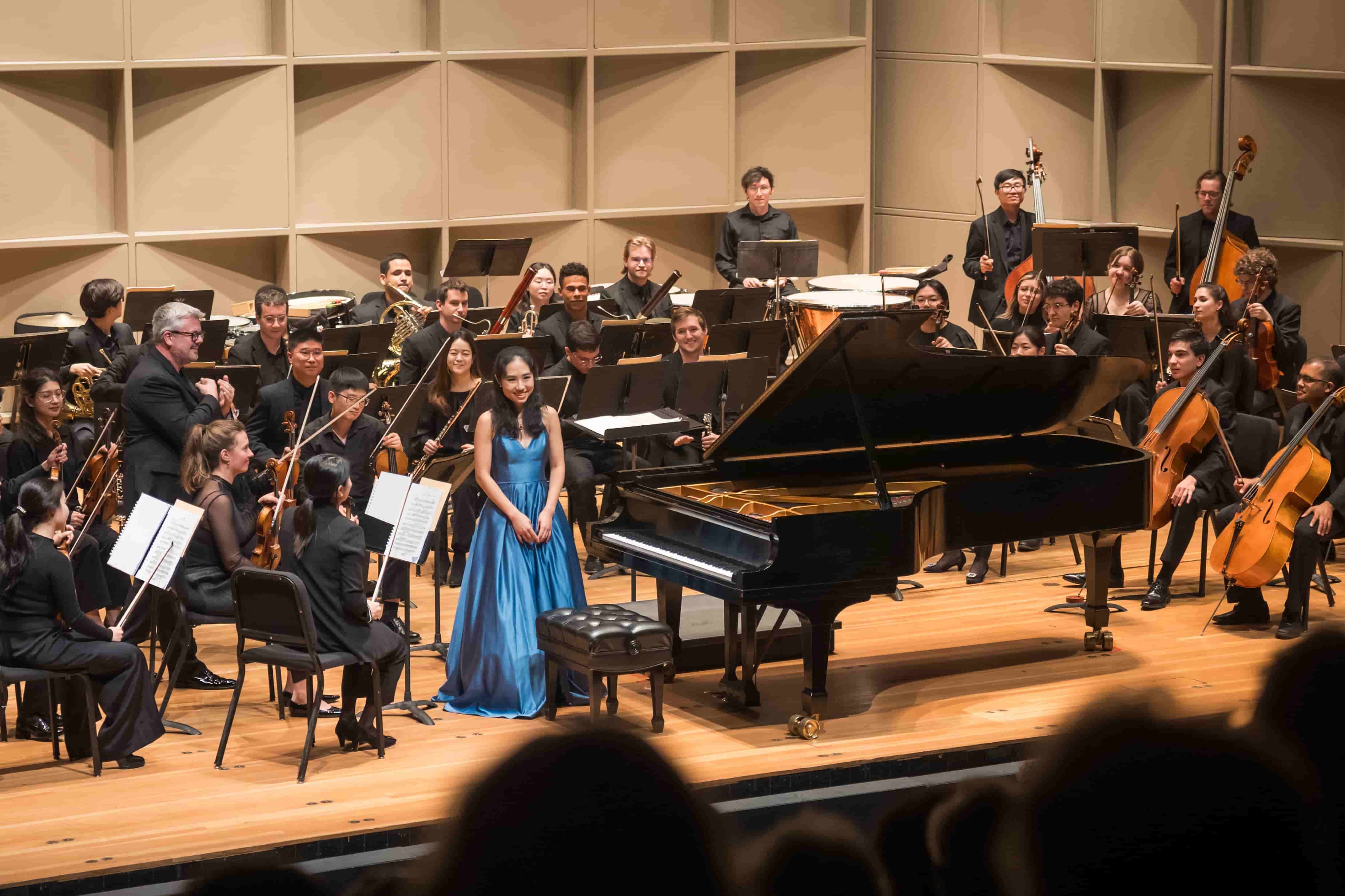 Minyi Zhang standing beside a grand piano in front of the orchestra after a performance.